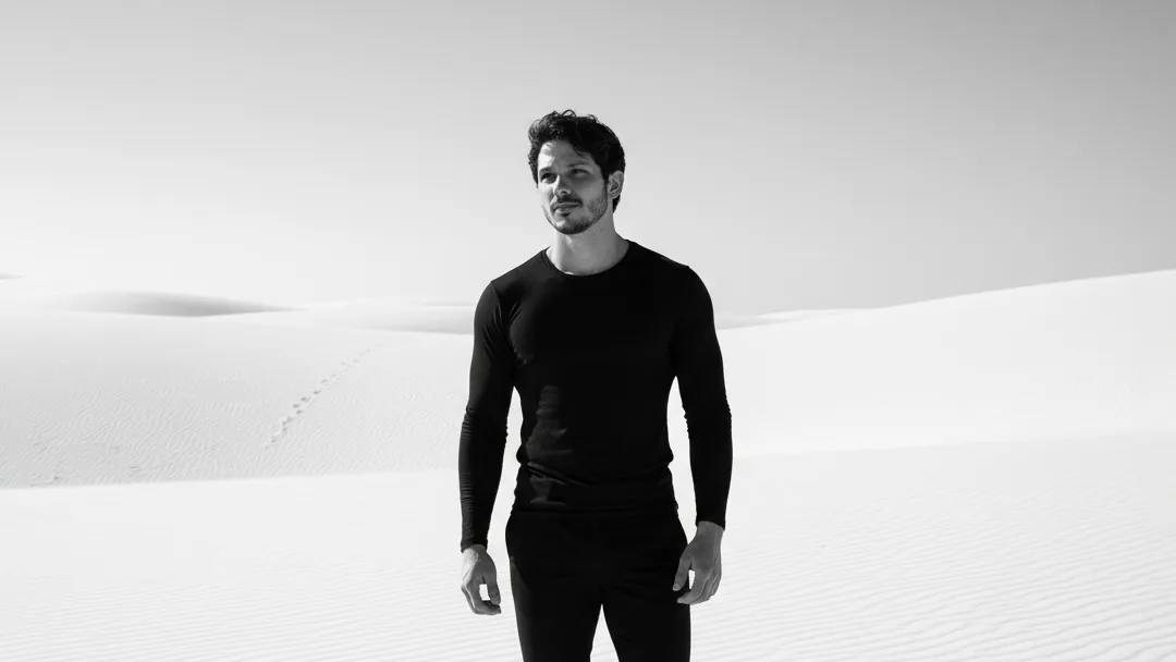 Evan Holfe em foto de presskit em preto e branco no deserto, recorte horizontal.