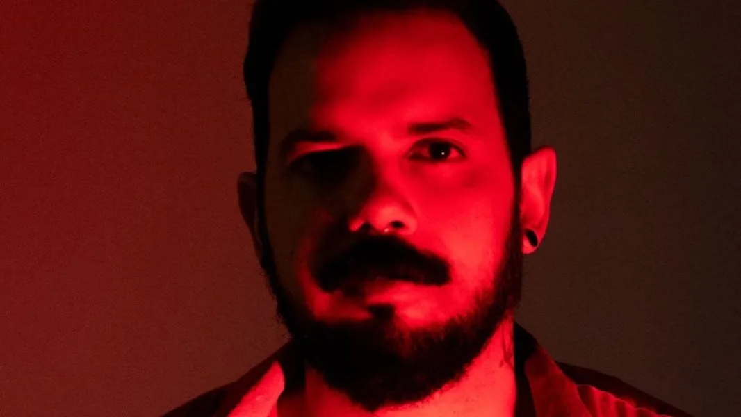 Infa Vermelho em retrato sob luz vermelha, com brincos e tatuagem no peito.